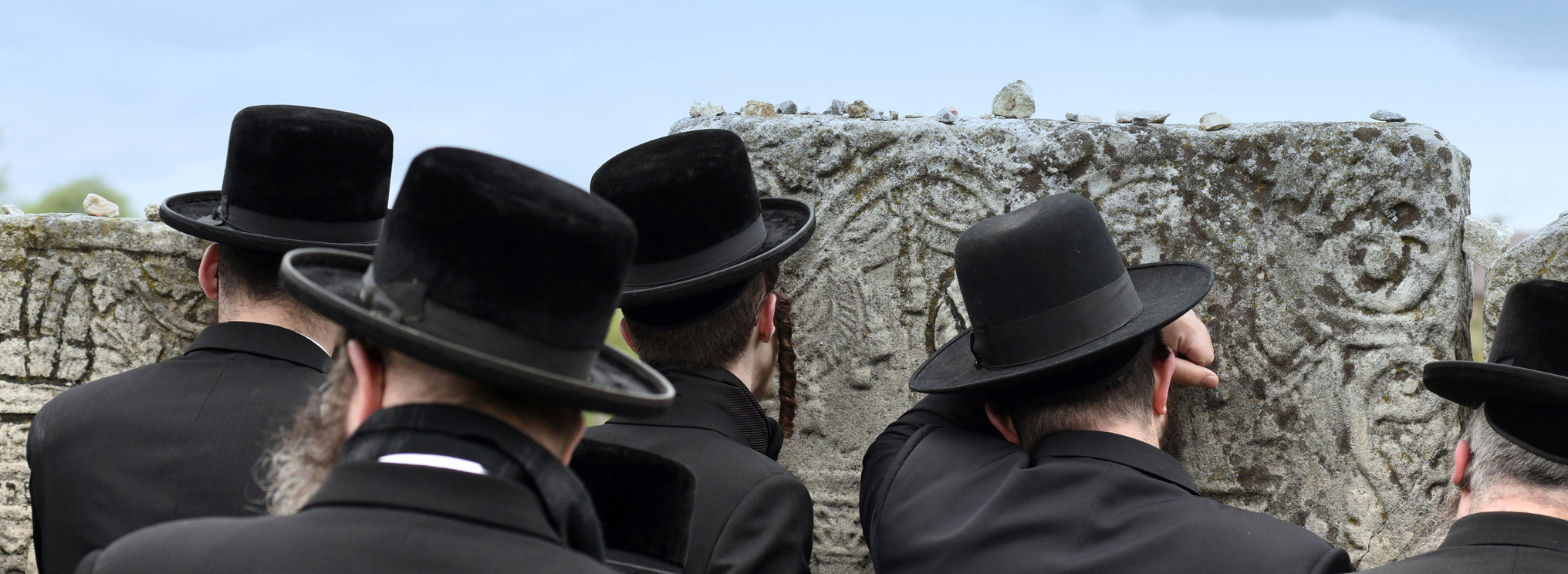 Rabbiner stehen vor einem Grabstein und gedenken Verstorbener. Das Bild verdeutlicht die rituelle Bedeutung von Erinnerung im Judentum.