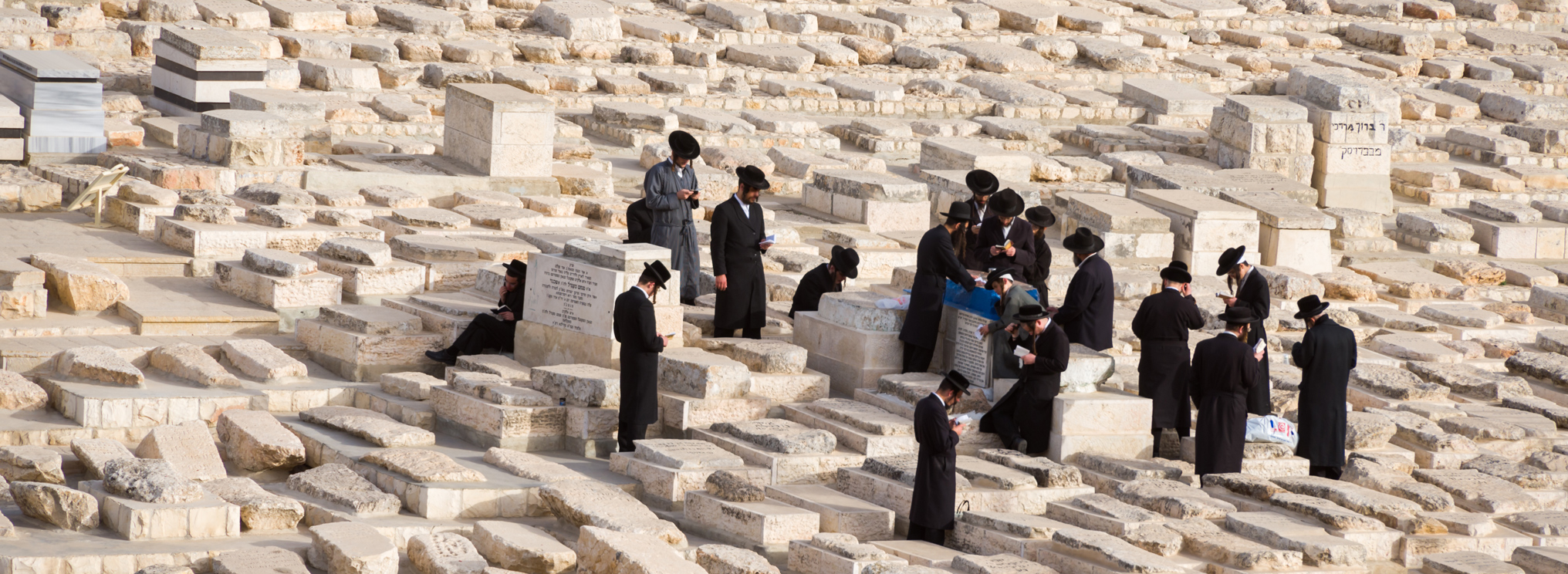 Rabbiner beten auf einem jüdischen Friedhof. Die Szene verweist auf traditionelle Rituale und Trauer im jüdischen Glauben.
